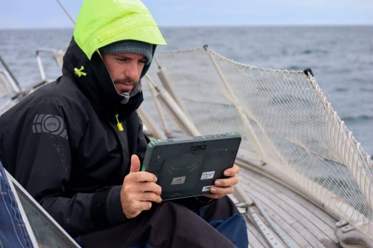 Sailor holding a SailProof tablet while controlling the boat's direction.