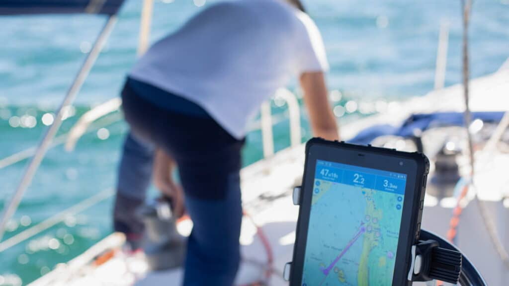 Tableta SailProof che mostra la navigazione a bordo di un veliero mentre lo skipper esegue una manovra in mare.